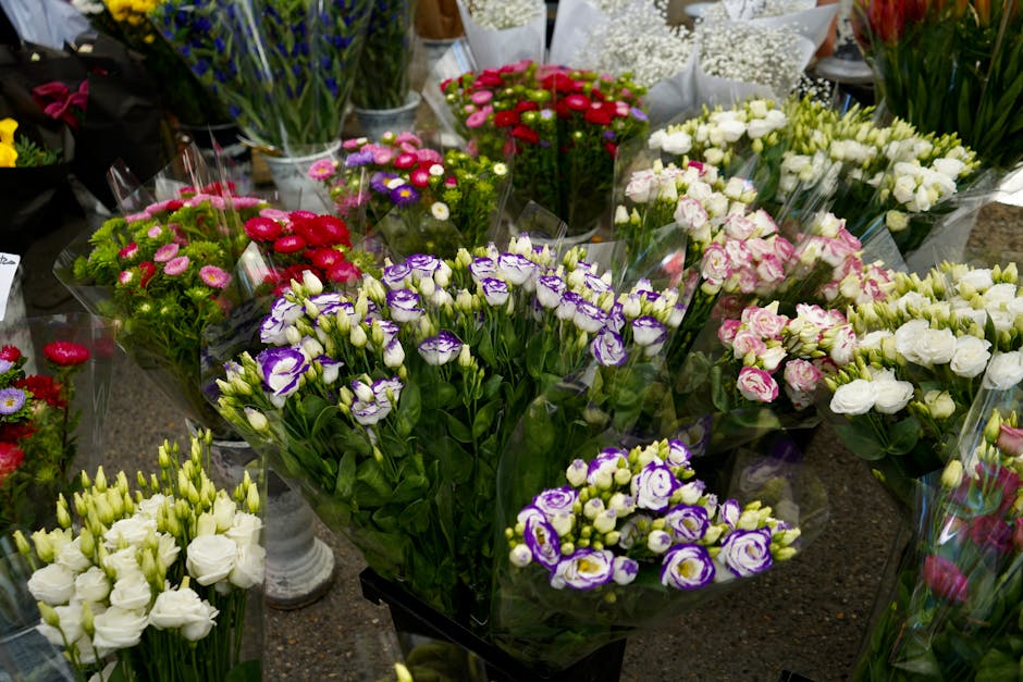 A vibrant display of freshly cut floral bouquets on a market stand, featuring a variety of flowers including white lisianthus, purple and white irises, pink and white roses, red and pink dahlias, and