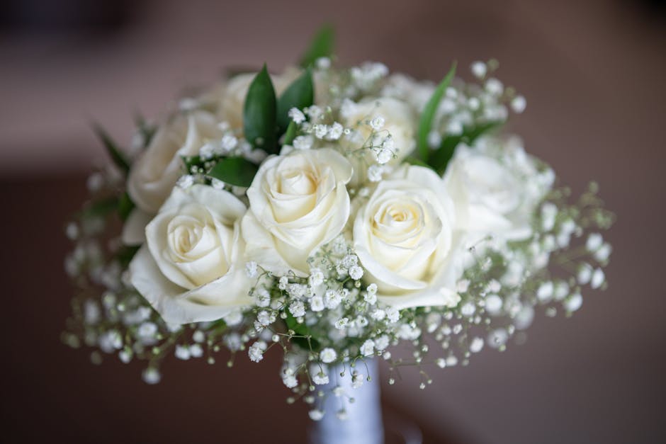 A close-up image of a wedding bouquet arranged by Gospel Oak florist, featuring creamy white roses with softly curled petals, accented by sprigs of delicate white baby's breath and lush green foliage.