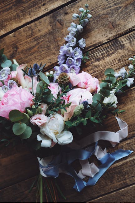 A wedding bouquet arrangement featuring large, soft pink peonies, white and light purple lisianthus, and sprigs of eucalyptus with rounded, green leaves. The flowers are arranged with varying textures