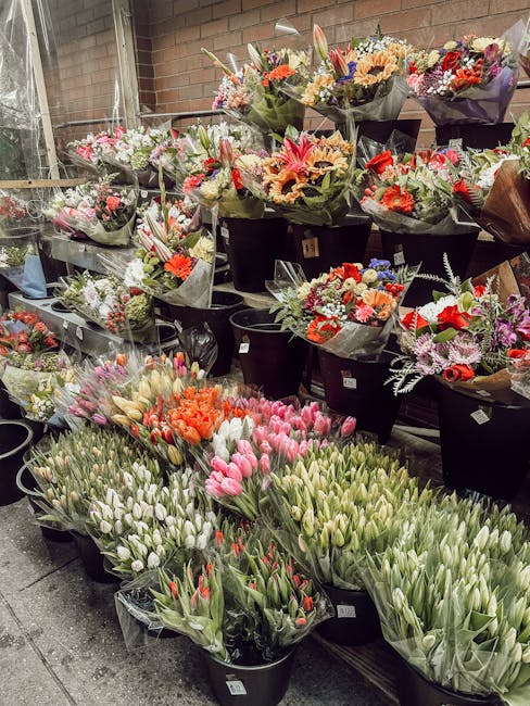 A large selection of fresh flower bouquets arranged in black buckets, featuring a variety of flowers including pink, white, red, orange, and purple blooms. The bouquets contain tulips, daisies, lilies